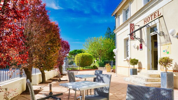 Un hotel con terraza, un letrero y un jardín cuidado.