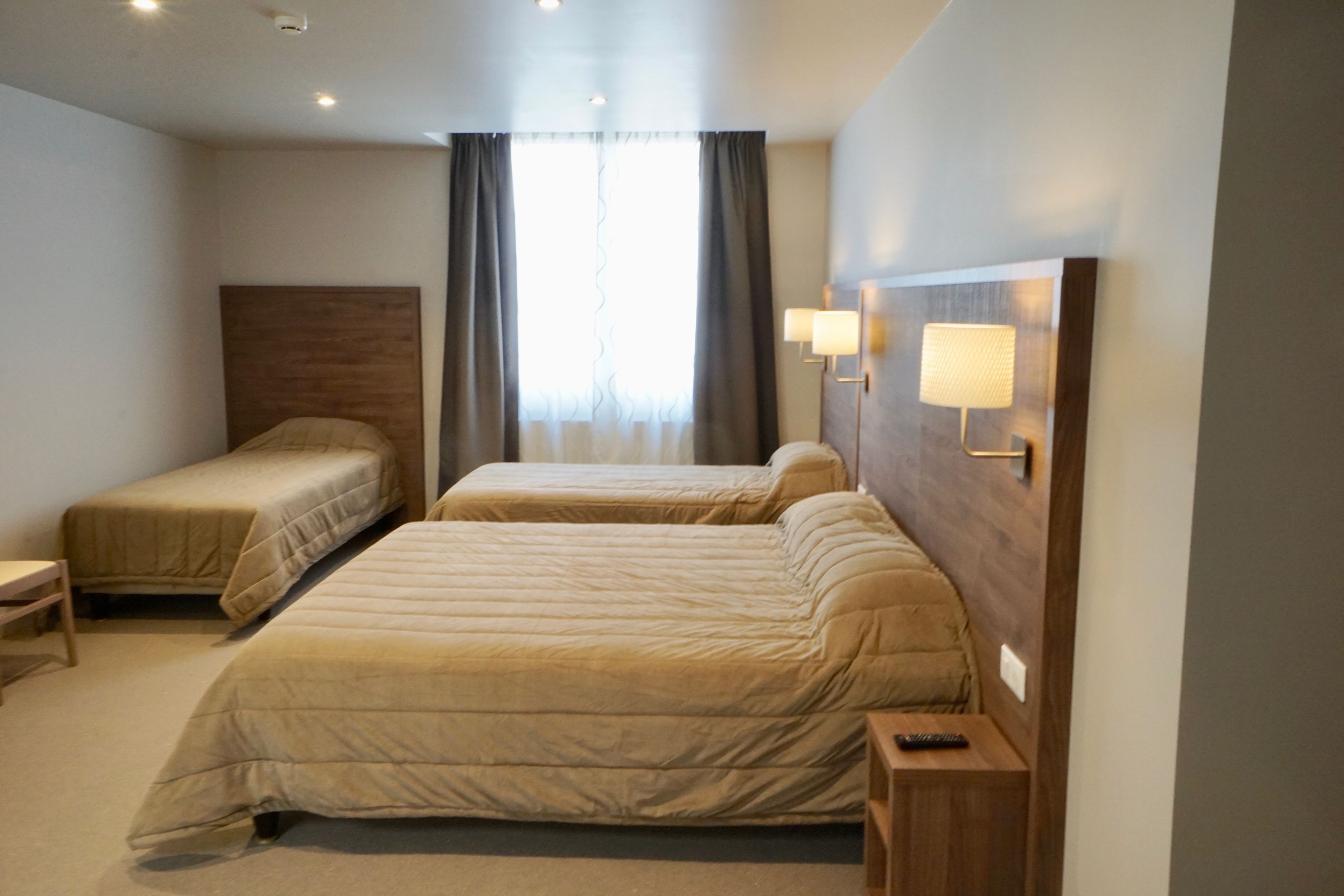 Habitación de hotel con dos camas, una mesita de noche, una lámpara y una ventana con cortinas.
