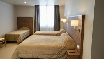 Habitación de hotel con dos camas, una mesita de noche, una lámpara y una ventana con cortinas.
