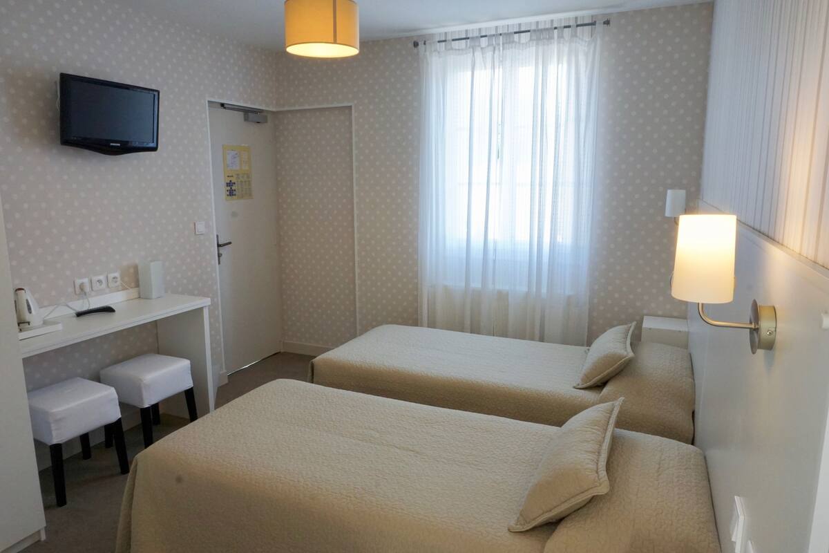 A hotel room with two beds, a desk with a chair, a television, and a window with curtains.