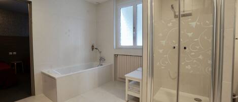 A modern bathroom with a bathtub, a glass-enclosed shower, and a small window.