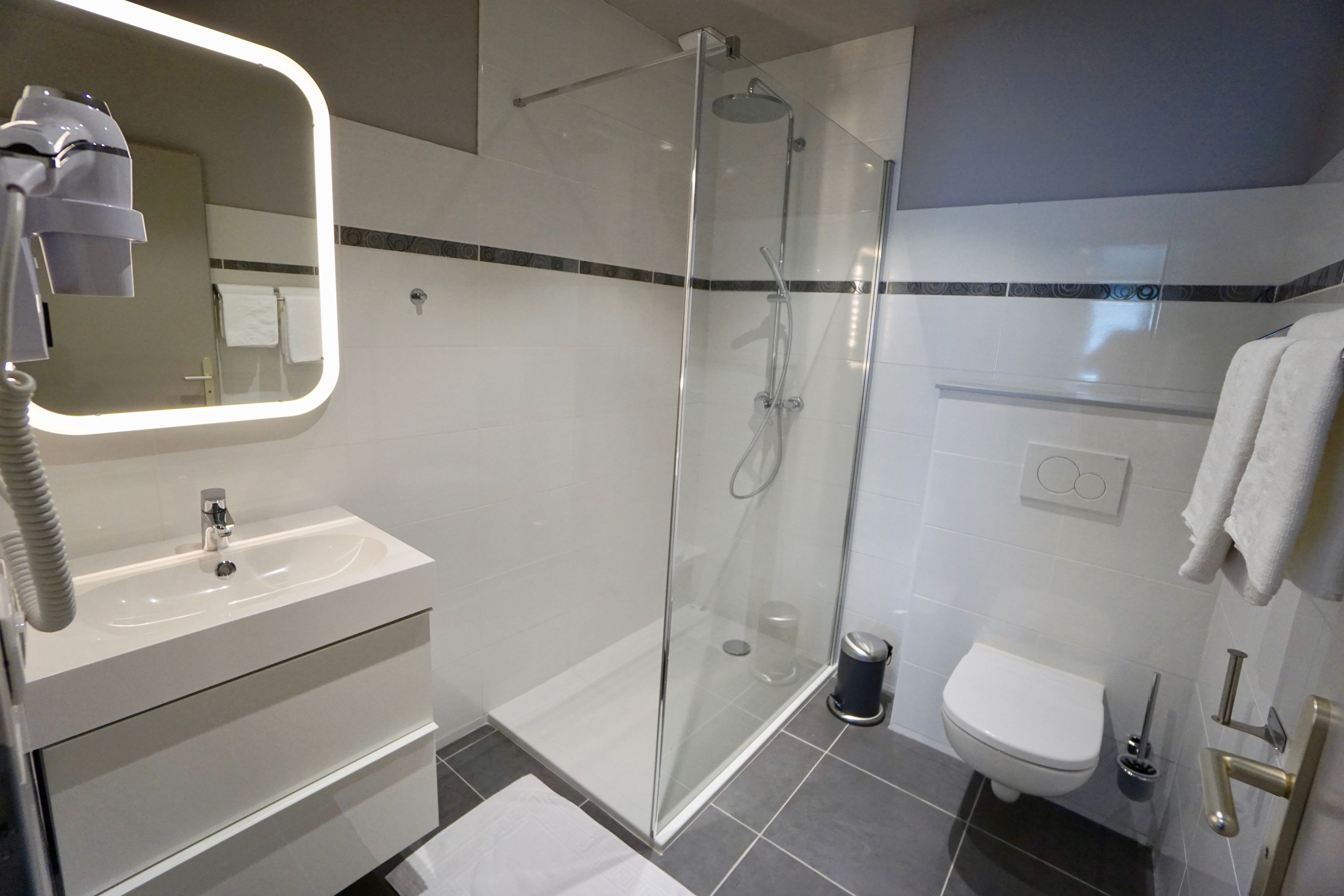 Une salle de bain moderne avec une douche à parois de verre, un lavabo blanc et des toilettes.