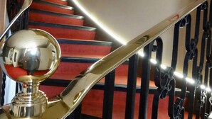 Una escalera con peldaños alfombrados de rojo y una barandilla metálica brillante.