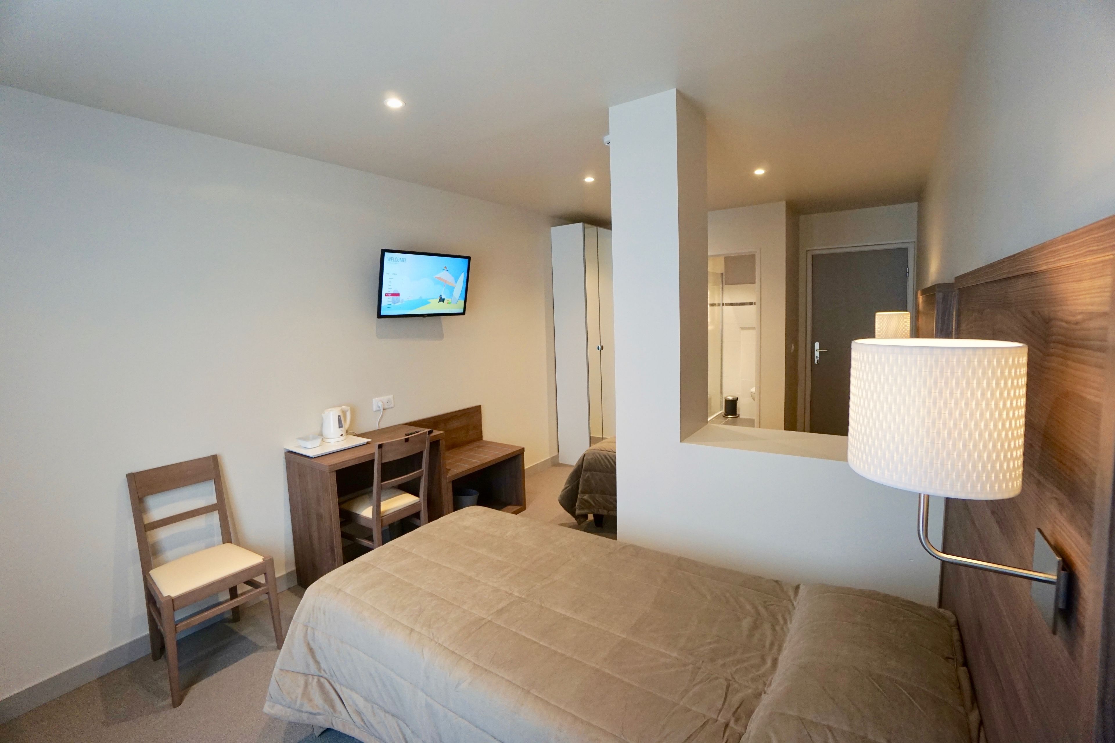Una habitación de hotel con cama, escritorio, silla, televisor y lámpara.