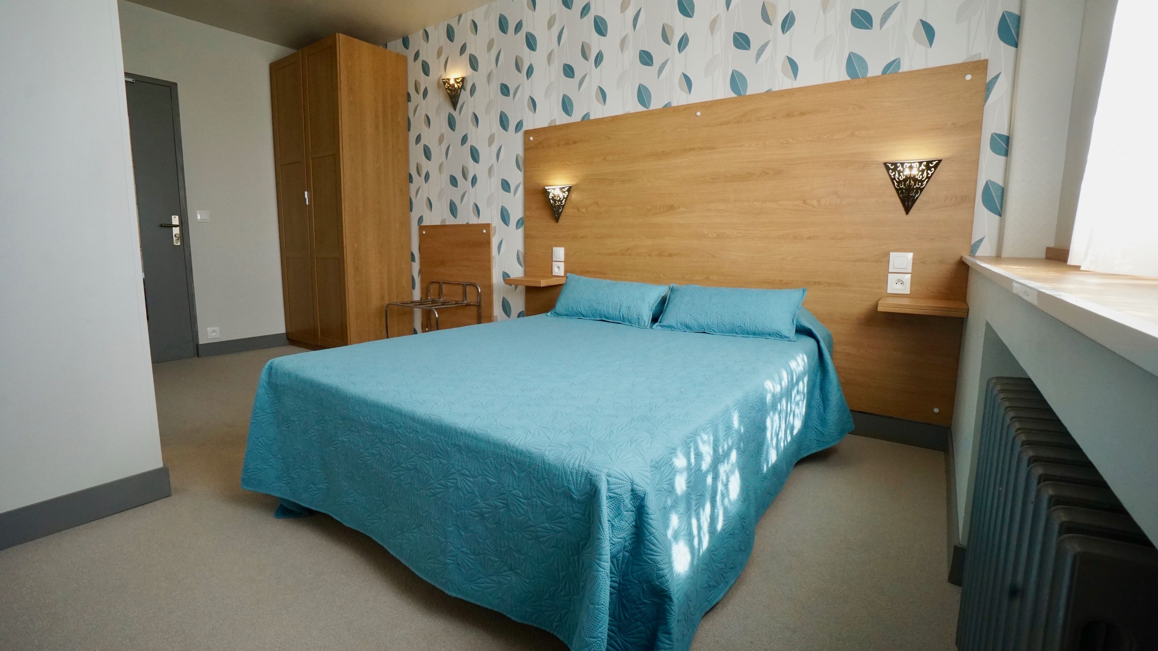Un dormitorio con cama, armario de madera y cabecera con luces fijadas a la pared.