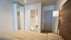 Un dormitorio con cama, cabecera de madera, espejo, una puerta y zona de ducha.