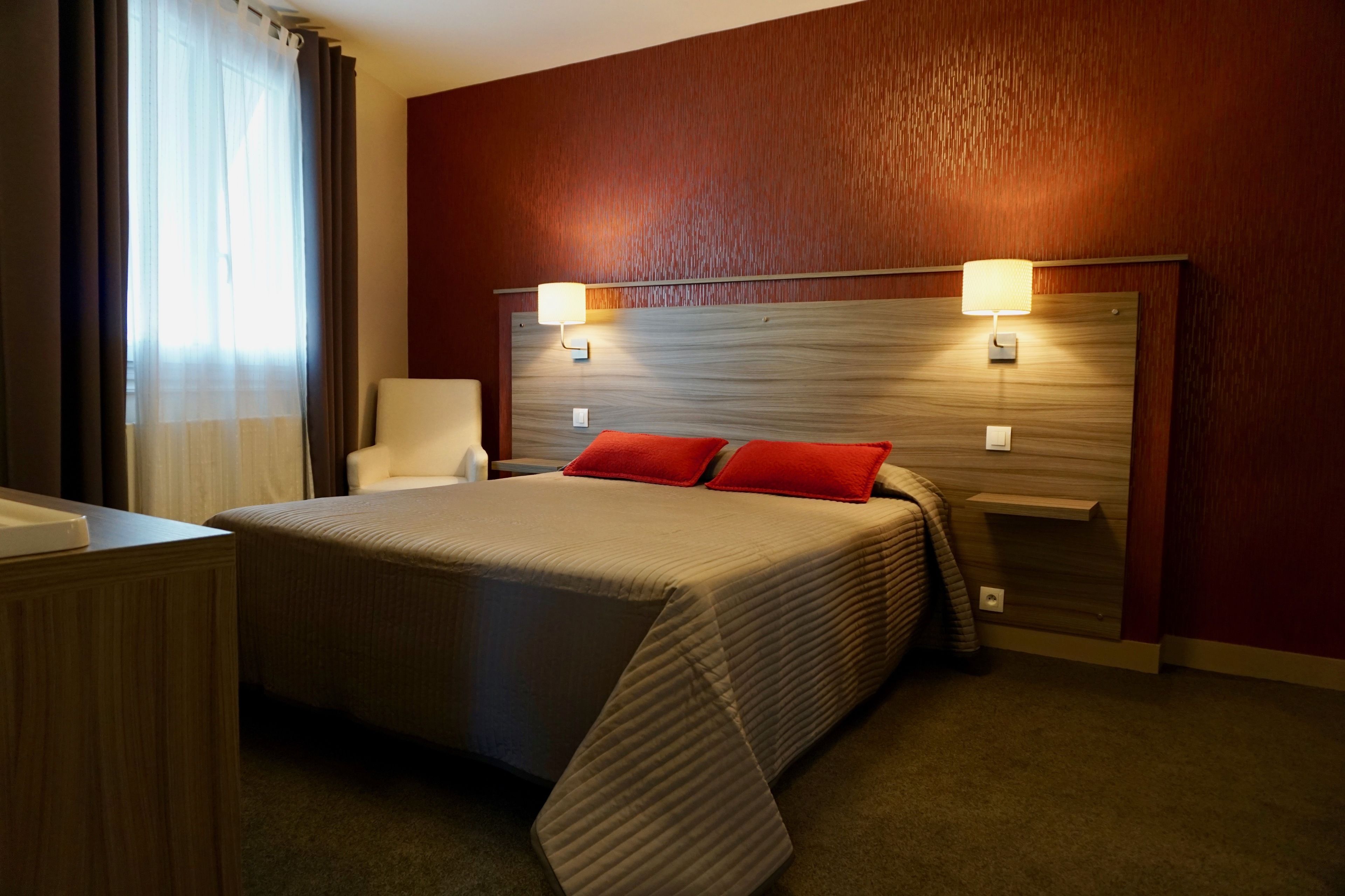 Une chambre d’hôtel avec un grand lit, deux lampes de chevet, une tête de lit en bois et une chaise.
