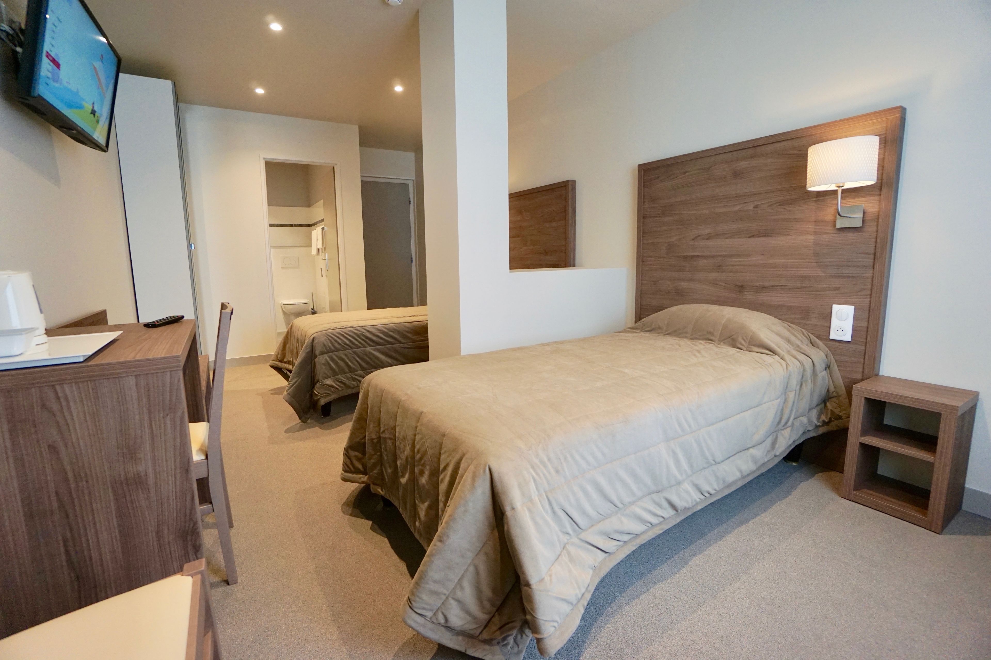 A hotel room with a bed, bedside table, TV, and a desk with a chair.