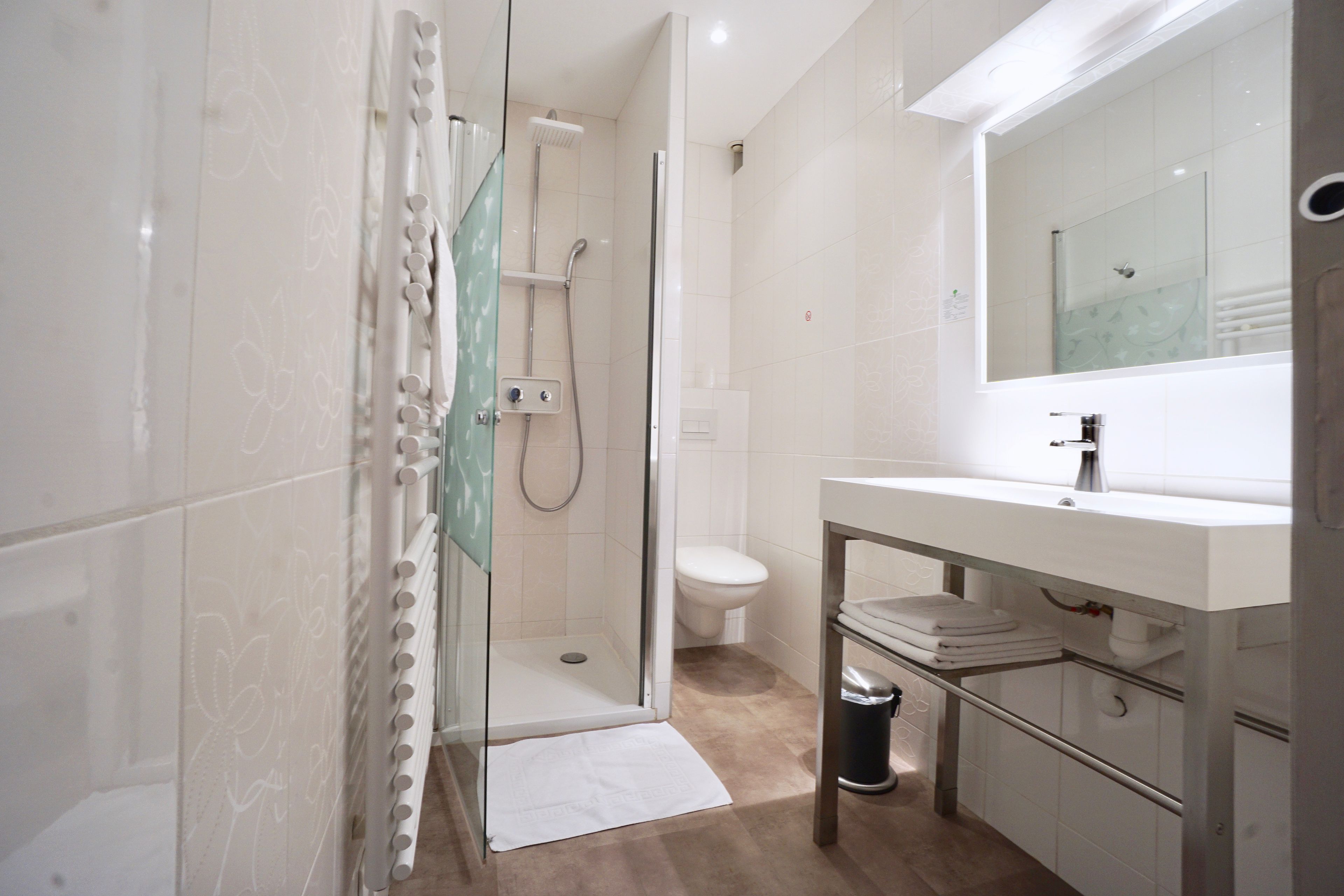 Een moderne badkamer met een douchecabine van glas, een witte wastafel en een grote spiegel.