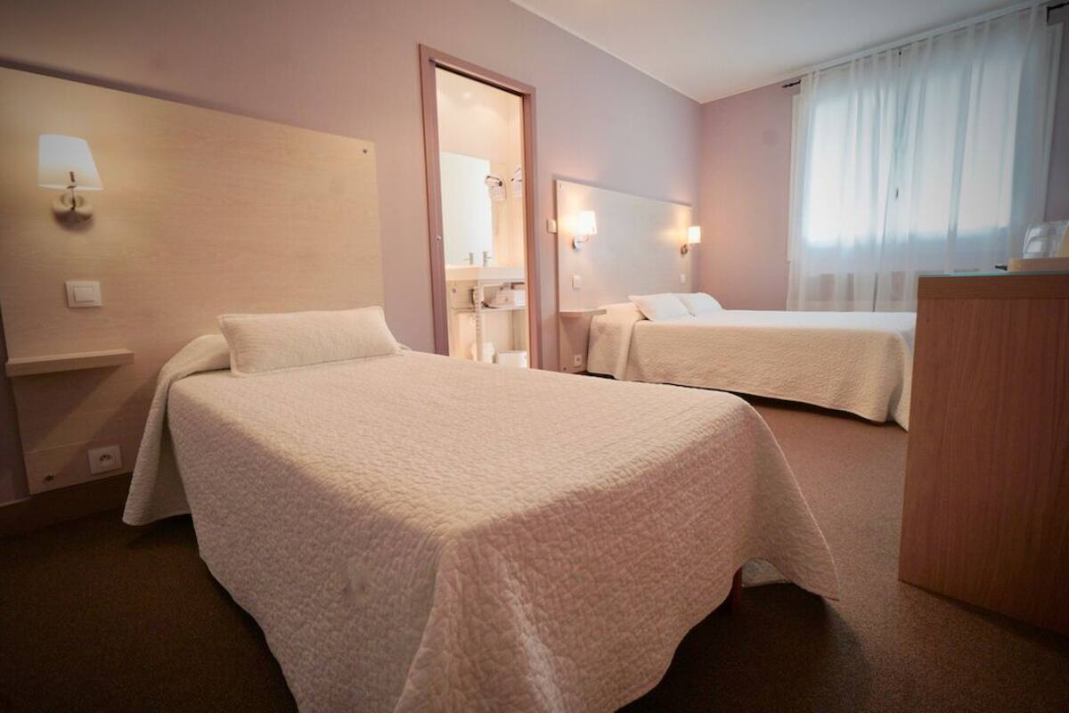 A hotel room with two beds, a wooden desk, a mirror, and wall-mounted lights.