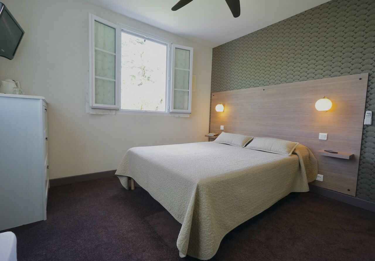 A bedroom with a bed, a window, a wall-mounted light, and a ceiling fan.