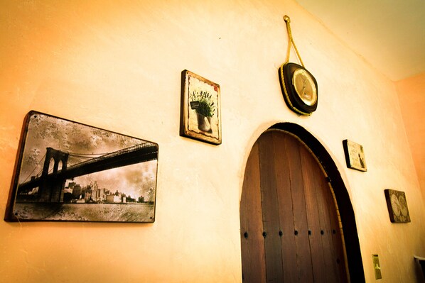 Una pared con un cuadro de un puente, una planta en maceta, un reloj y una puerta de madera.