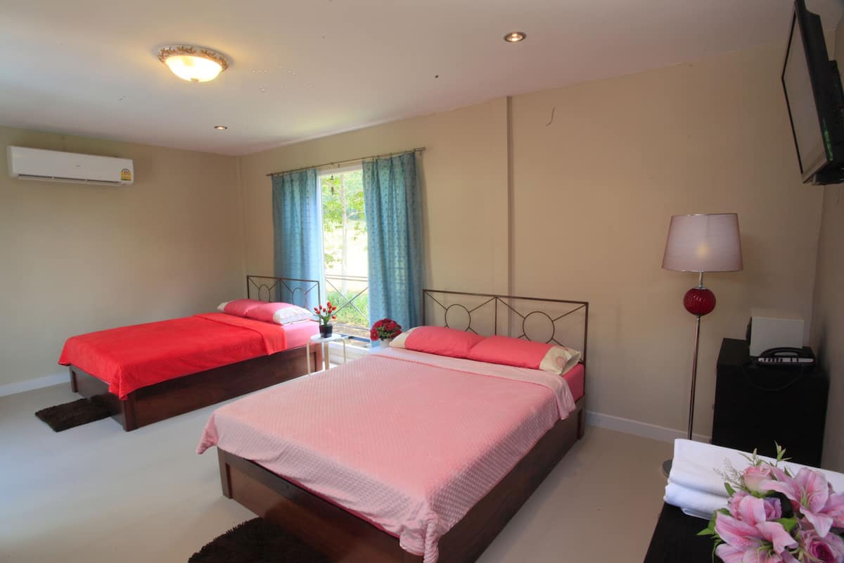 A hotel room with two beds, a window with curtains, an air conditioner, a bedside table with a lamp, and a TV on a stand.