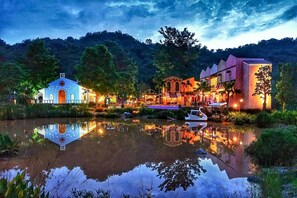 Hotel junto al lago con su reflejo en el agua, destacando una embarcación con forma de cisne, un área de comedor y un edificio grande con balcón.