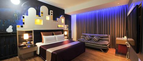 Una habitación de hotel moderna con una cama grande, un escritorio con lámpara, un televisor montado en la pared y una ventana con cortinas.