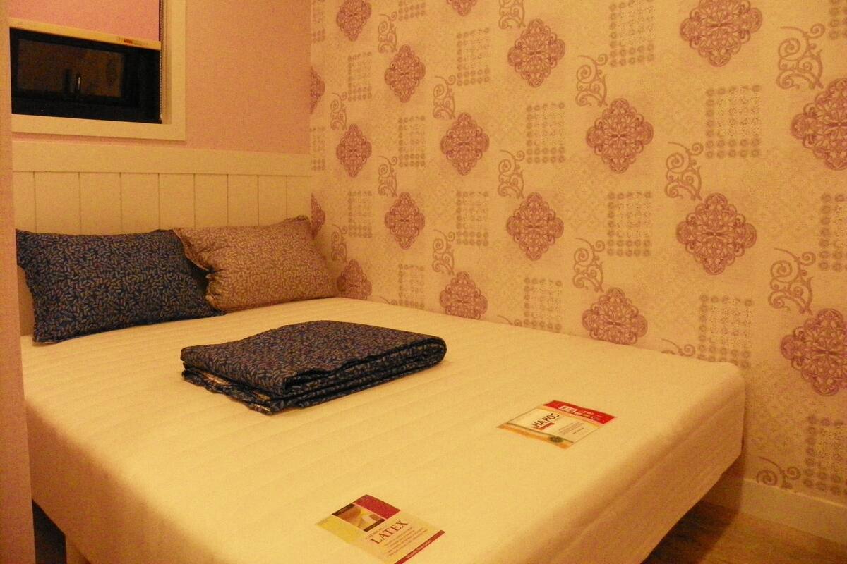 Una cama individual con una pared estampada y una ventana encima.