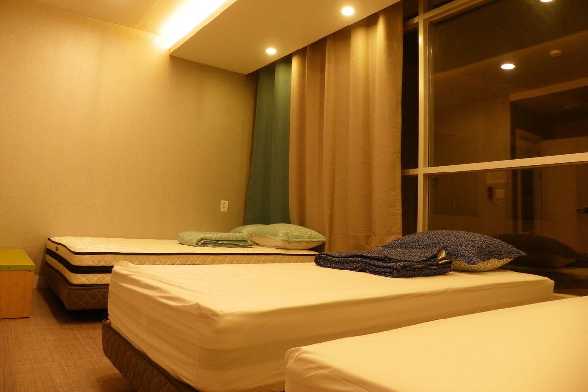 Habitación de hotel con dos camas, una ventana con cortinas y suelo de madera.