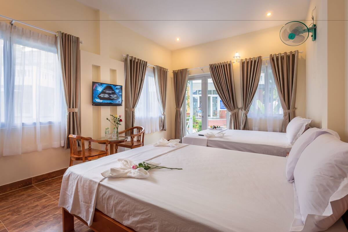 A hotel room with two beds, a TV, a dining table with chairs, and a window with curtains.