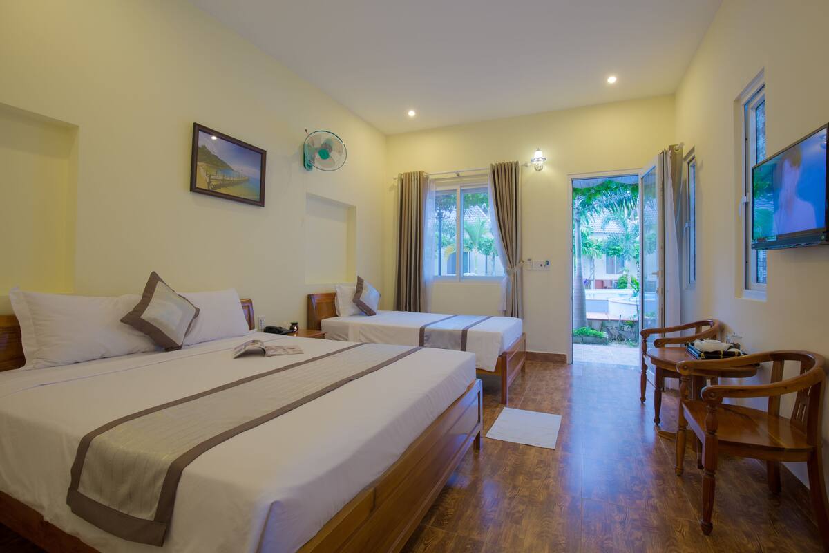 A hotel room with two beds, a TV, a desk, and a view of the outdoors.