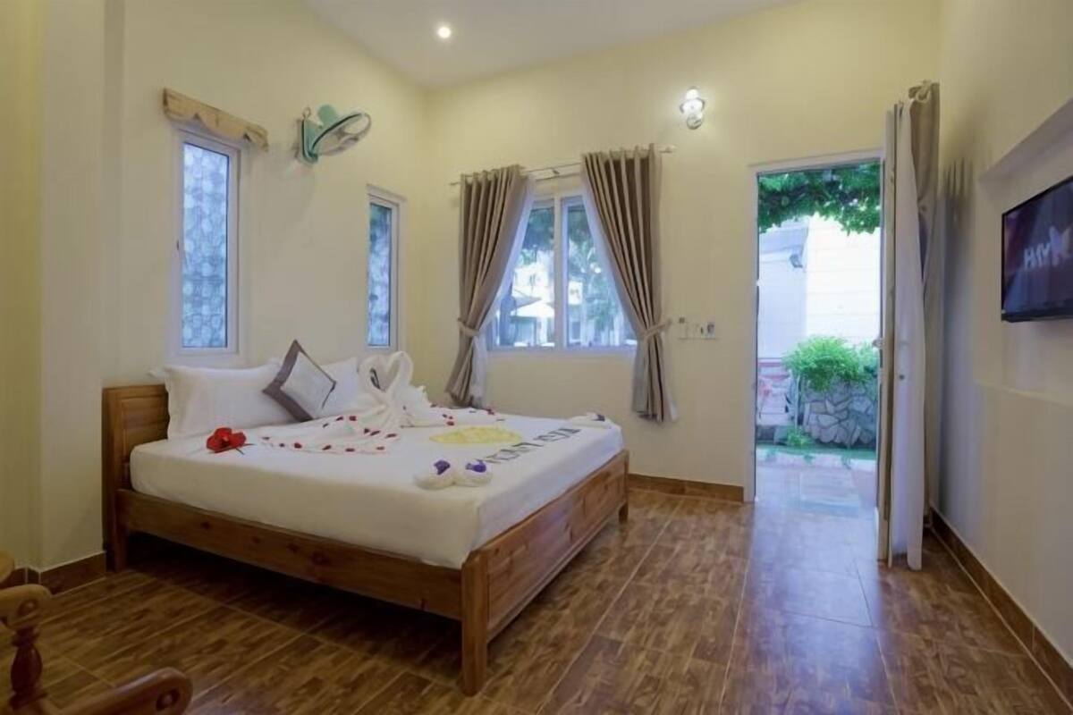 A bedroom with a wooden bed, two windows, a door leading outside, and a TV on the wall.