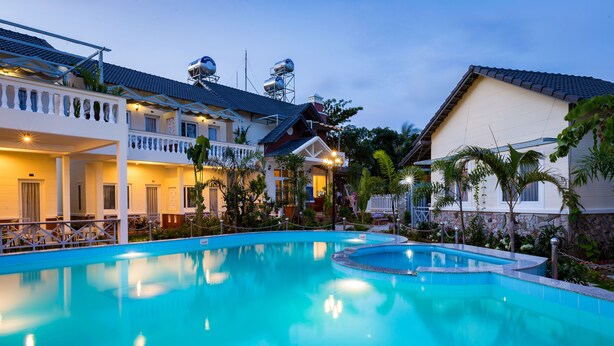 A swimming pool with a curved design, surrounded by buildings with balconies and a covered area. - Blue Paradise Resort (Phu Quoc)