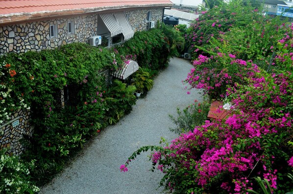 Un edificio de piedra con techo rojo, rodeado de exuberante follaje y flores rosadas.