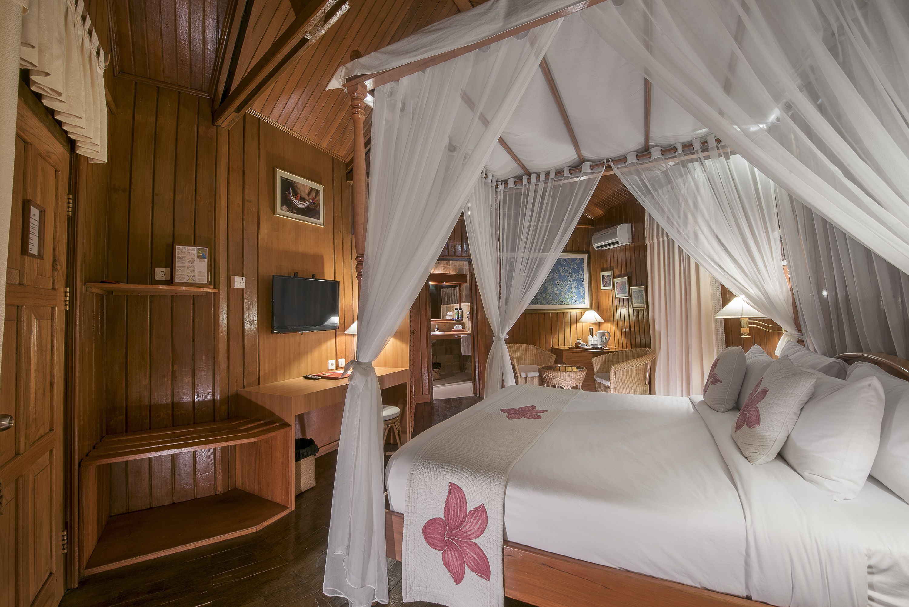 A bedroom with a canopy bed, wooden walls, a television, and a small desk.