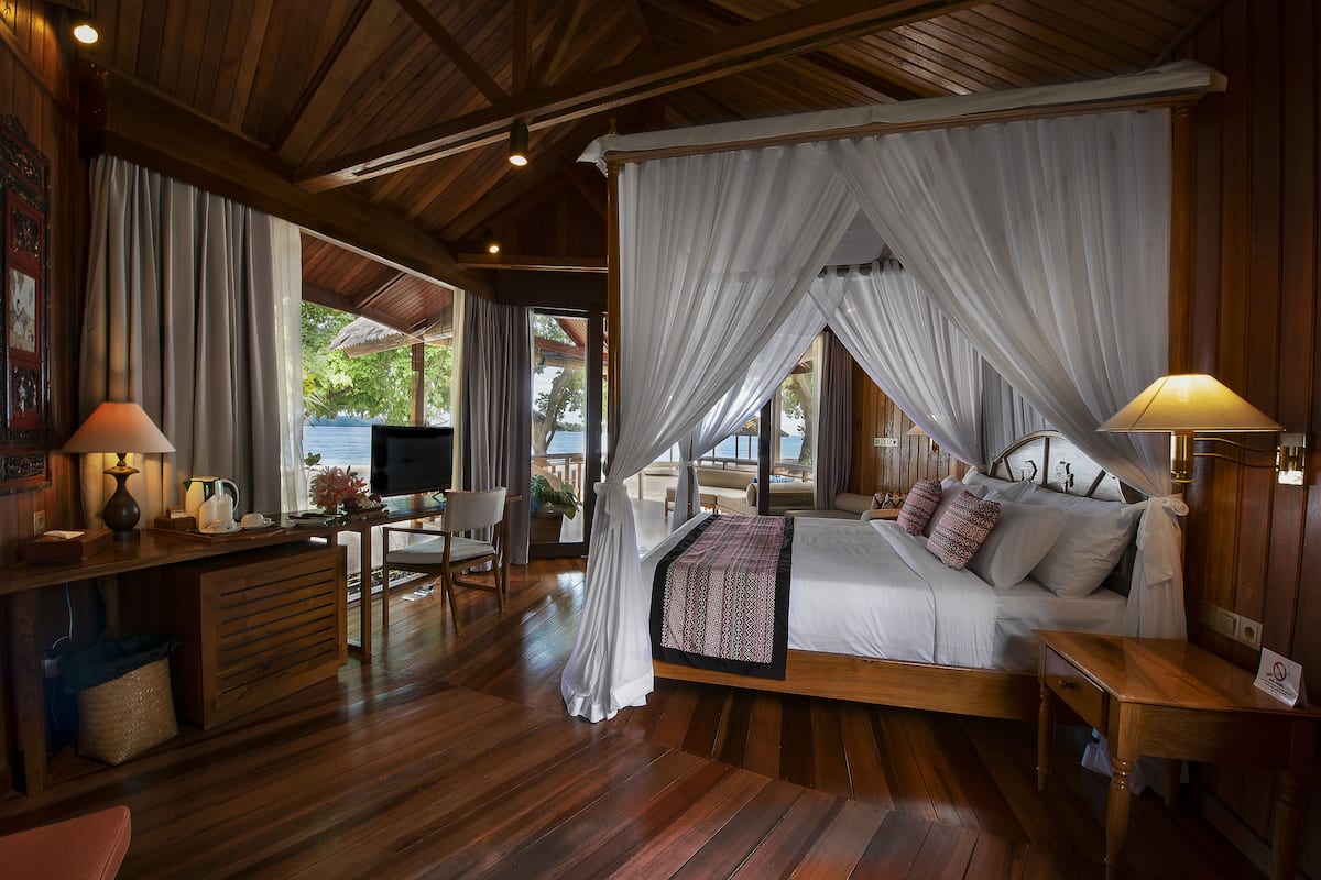 Une chambre spacieuse dotée d’un lit à baldaquin, de parquet et offrant une vue sur l’extérieur.
