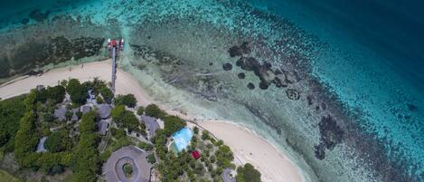 An aerial view of a coastal resort with a long pier, beach, and lush greenery.