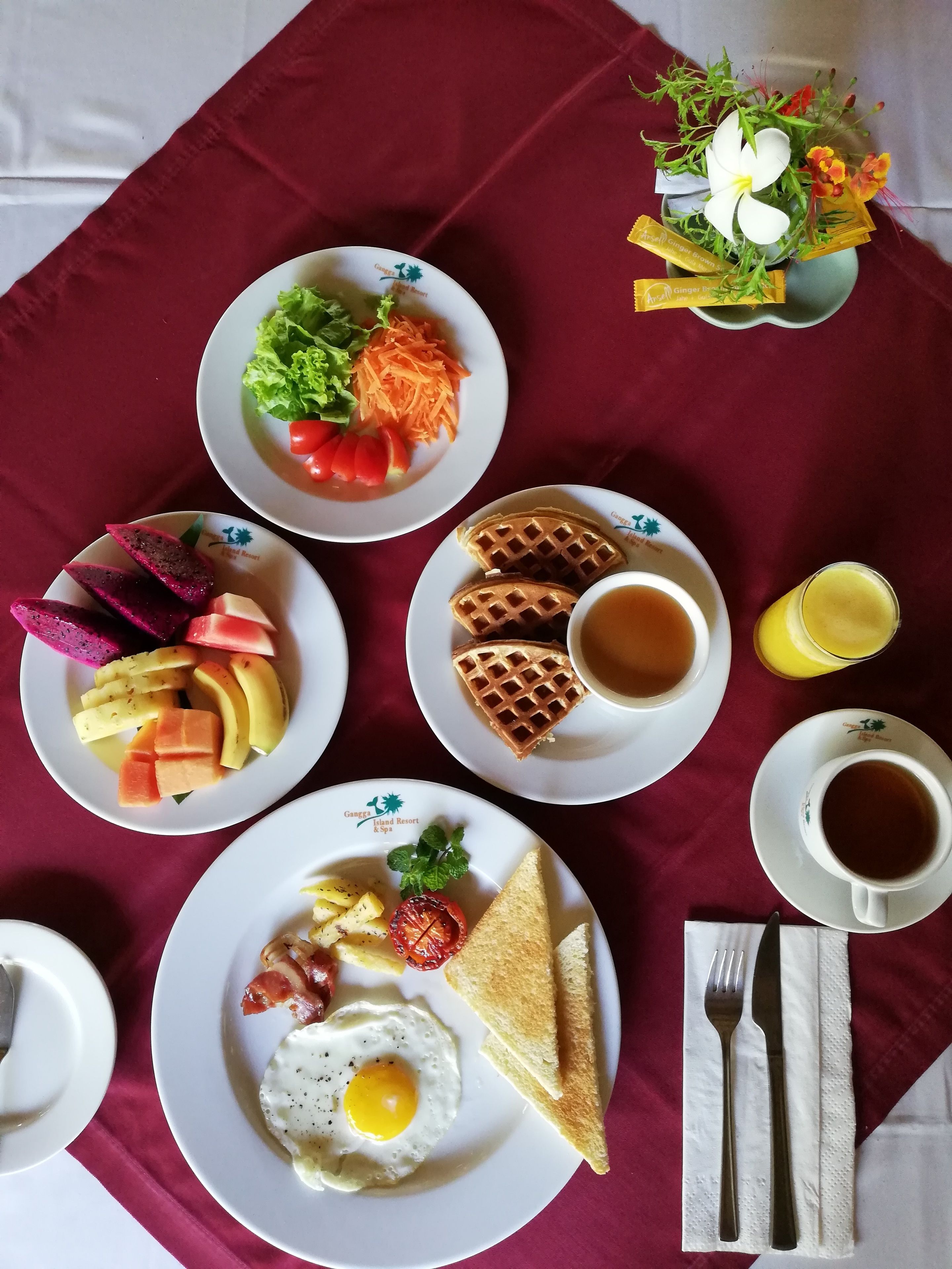 A breakfast spread with various dishes including waffles, eggs, toast, and fruit on a table with a red tablecloth.