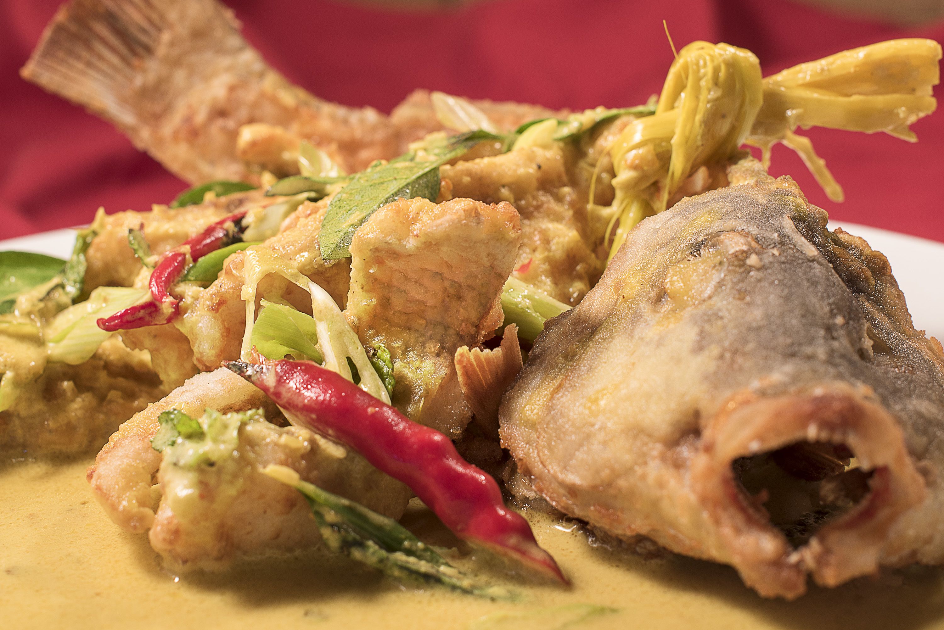 Un plato con pescado frito, verduras y salsa cremosa.