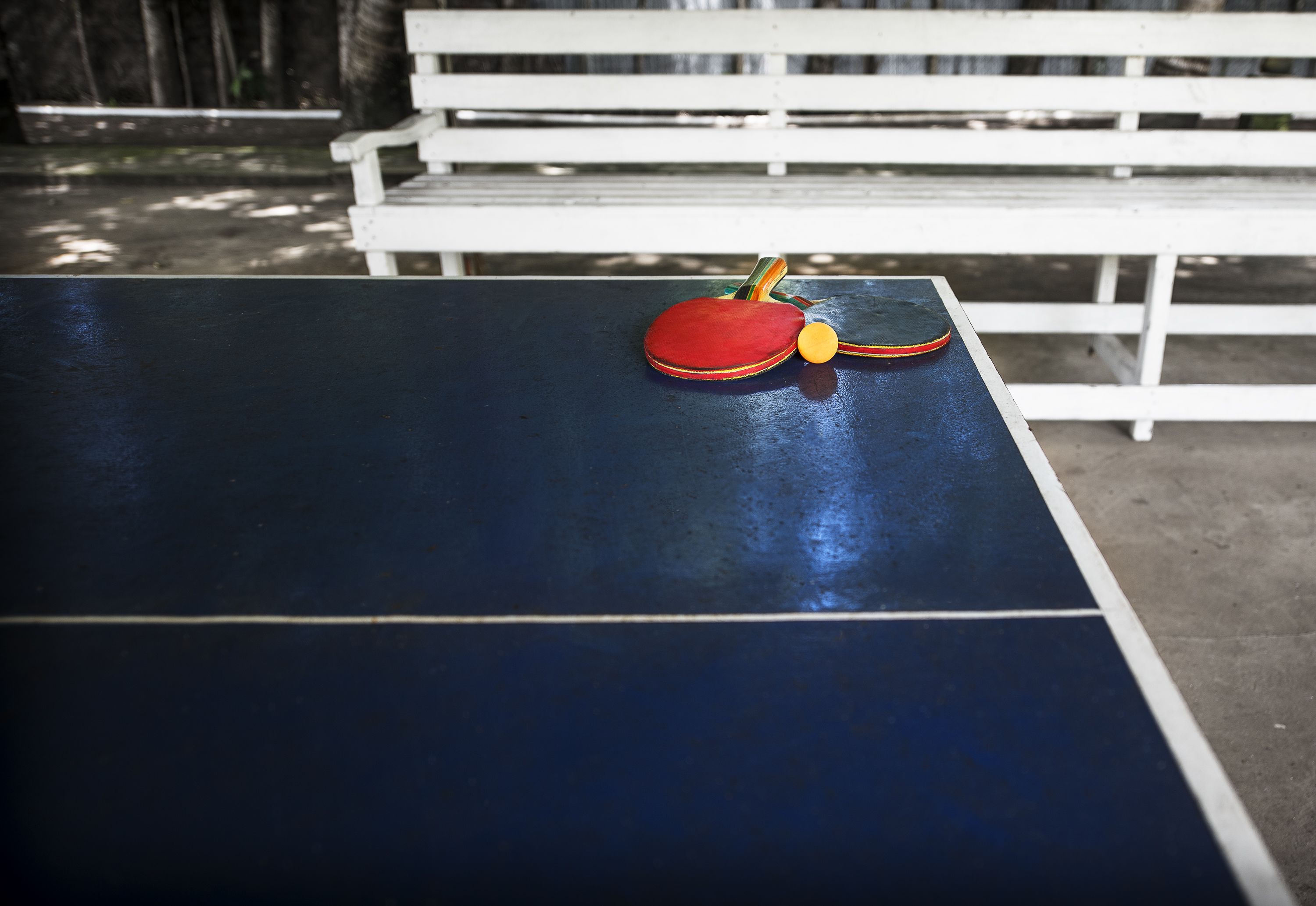 A ping pong table with a red and yellow paddle in front of a white bench.