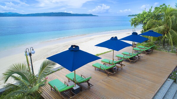 A wooden deck with green lounge chairs and blue umbrellas overlooking a beach with clear turquoise water and distant islands. - Gangga Island Resort & Spa (Pulau Gangga)