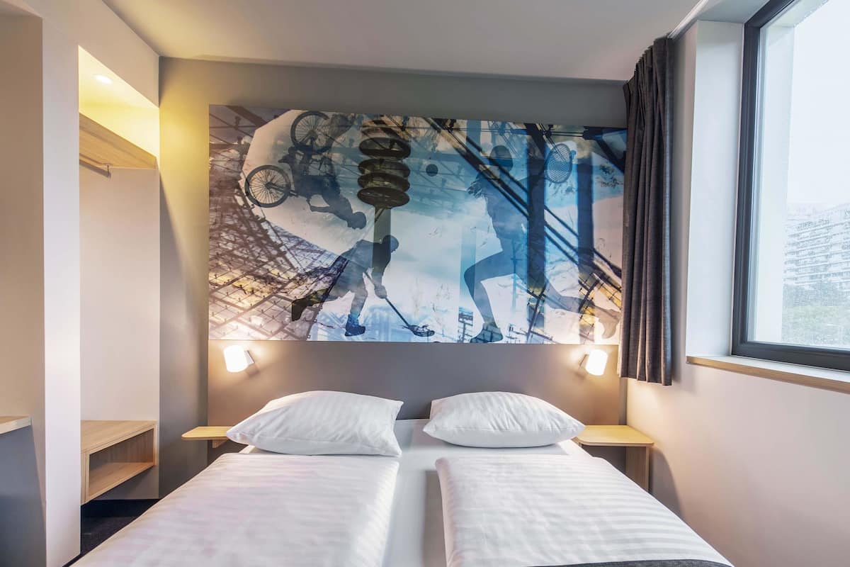Hotelkamer met een bed, twee nachtkastjes, een groot abstract kunstwerk aan de muur en een raam met gordijnen.