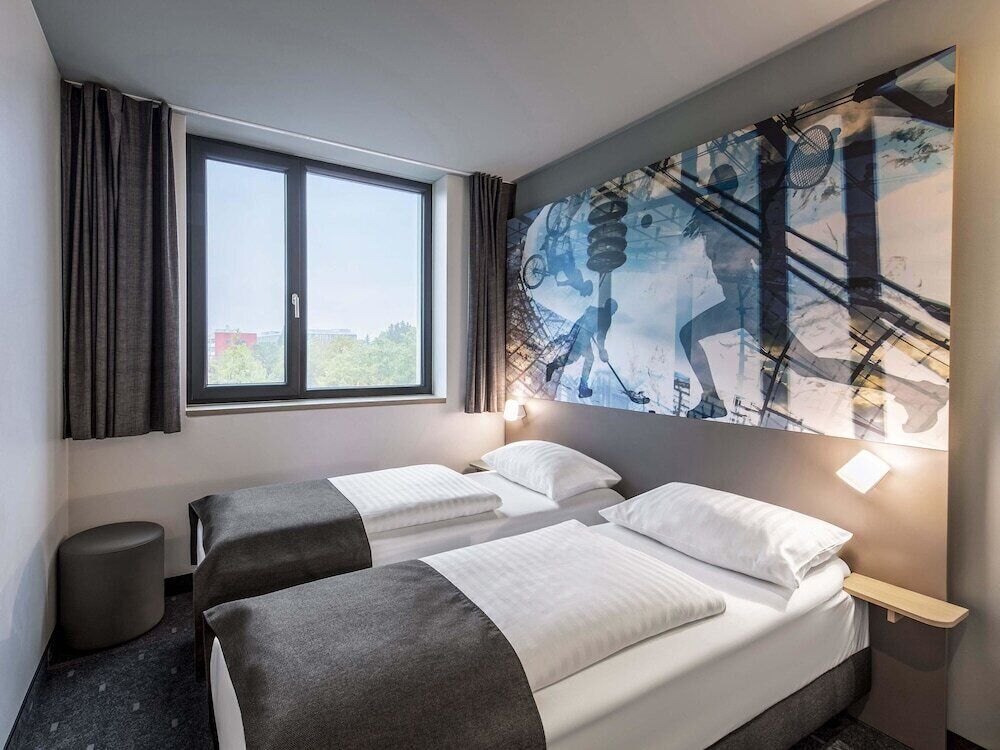 Une chambre d’hôtel avec deux lits, une grande fenêtre et une fresque murale.