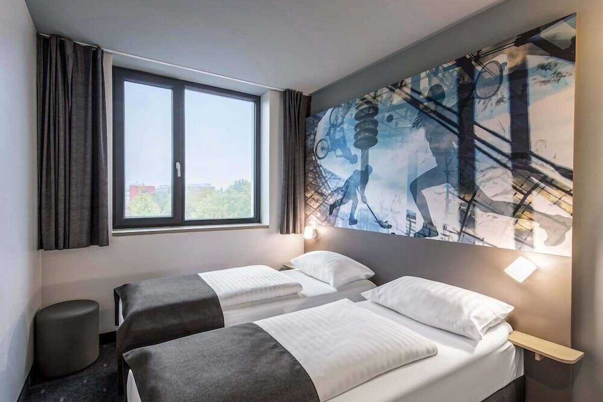 Een hotelkamer met twee bedden, een groot raam en een muurschildering.