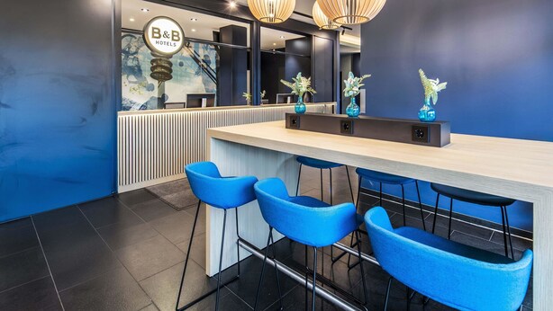 Un espace d’accueil moderne avec un comptoir, des tabourets de bar bleus et un éclairage décoratif.