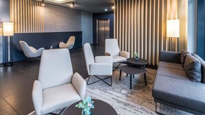 Un hall d’entrée moderne doté d’un espace détente avec des canapés et des fauteuils, un tapis à motifs et un mur orné de lattes de bois verticales.