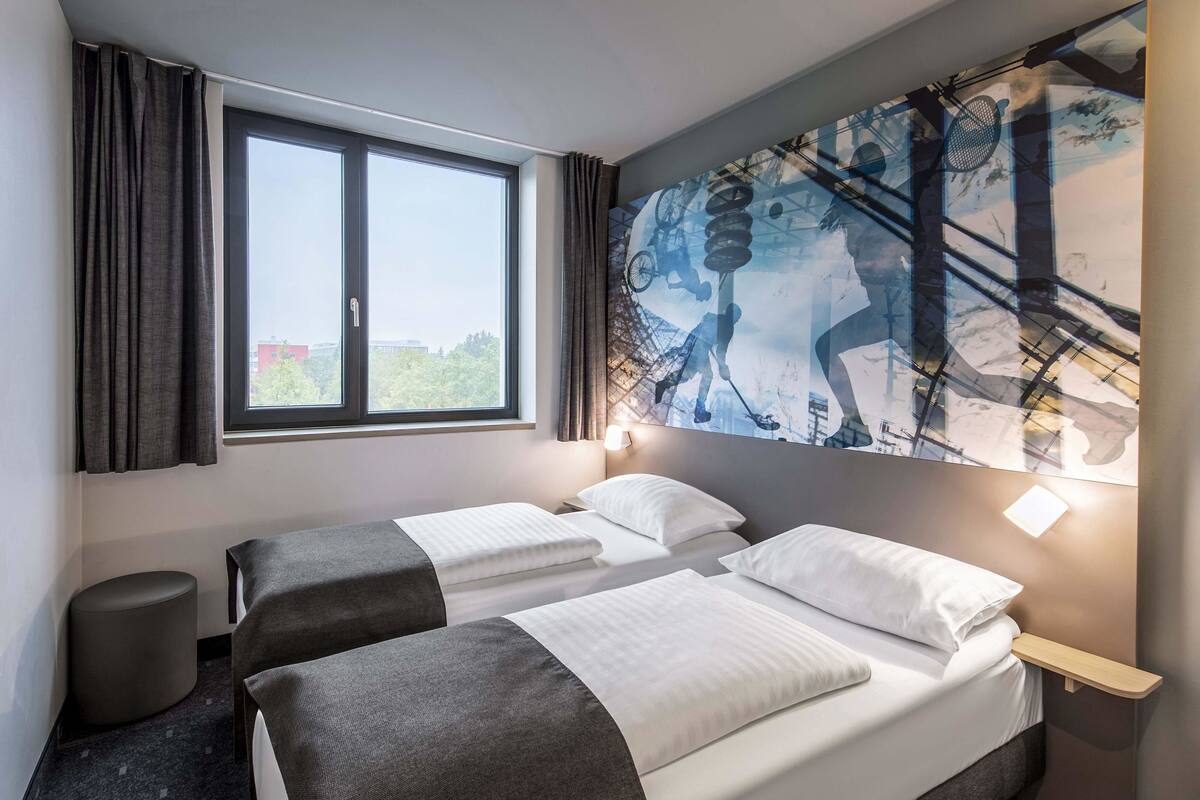 Een hotelkamer met twee bedden, een groot raam en een kunstwerk aan de muur.