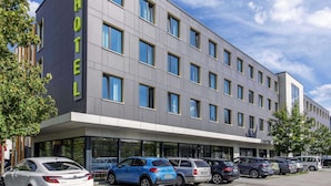 Un hôtel moderne, avec une façade plate, de nombreuses fenêtres et un parking où sont garées plusieurs voitures.