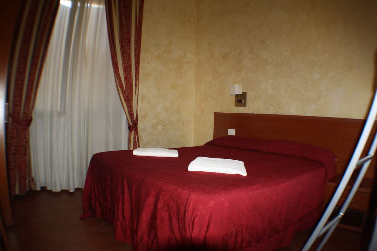 A hotel room with a large bed, a nightstand, a lamp, and a window with curtains.