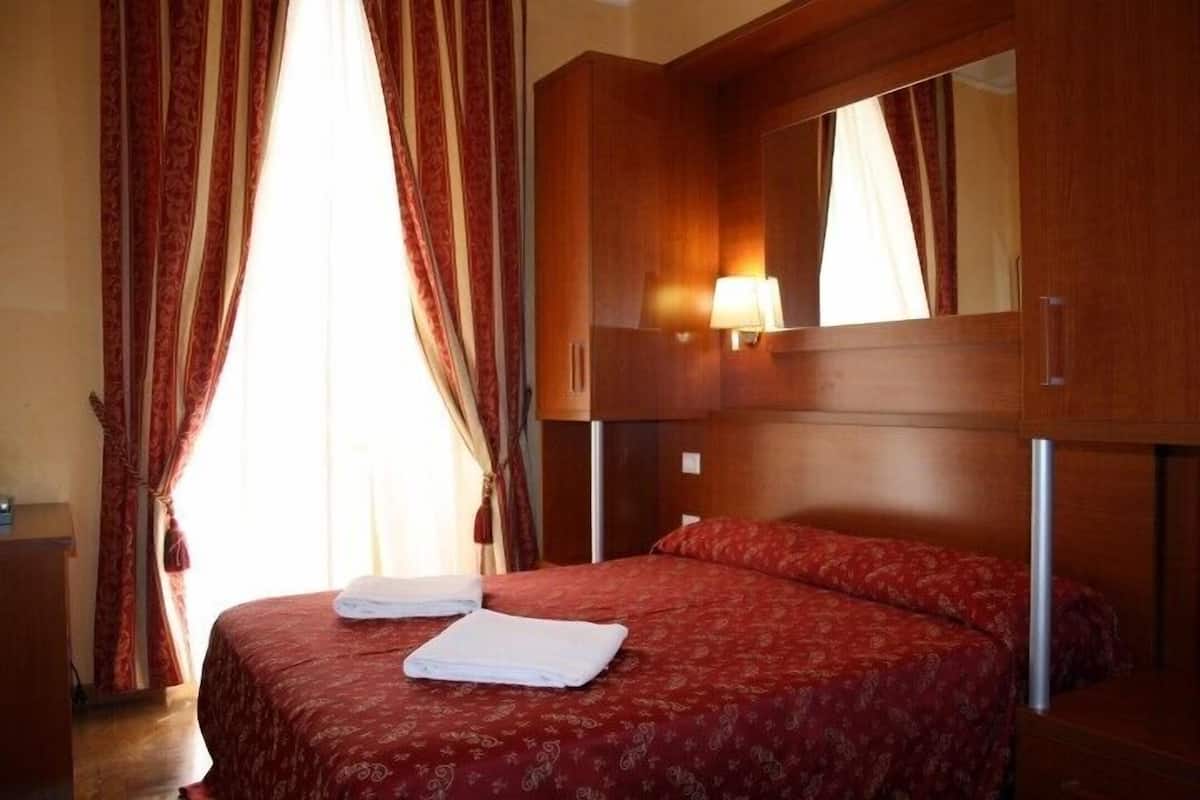 A hotel room with a large bed, a wooden headboard, a mirror, and a bedside lamp.
