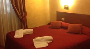Camera d'albergo con copripiumino rosso, due cuscini e due asciugamani piegati con cura.