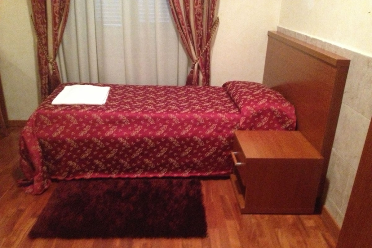 A small, neatly arranged bedroom with a bed, a wooden nightstand, and a small table.