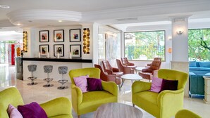 Un vestíbulo moderno con sillones verdes, una recepción, obras de arte enmarcadas y vistas al exterior.