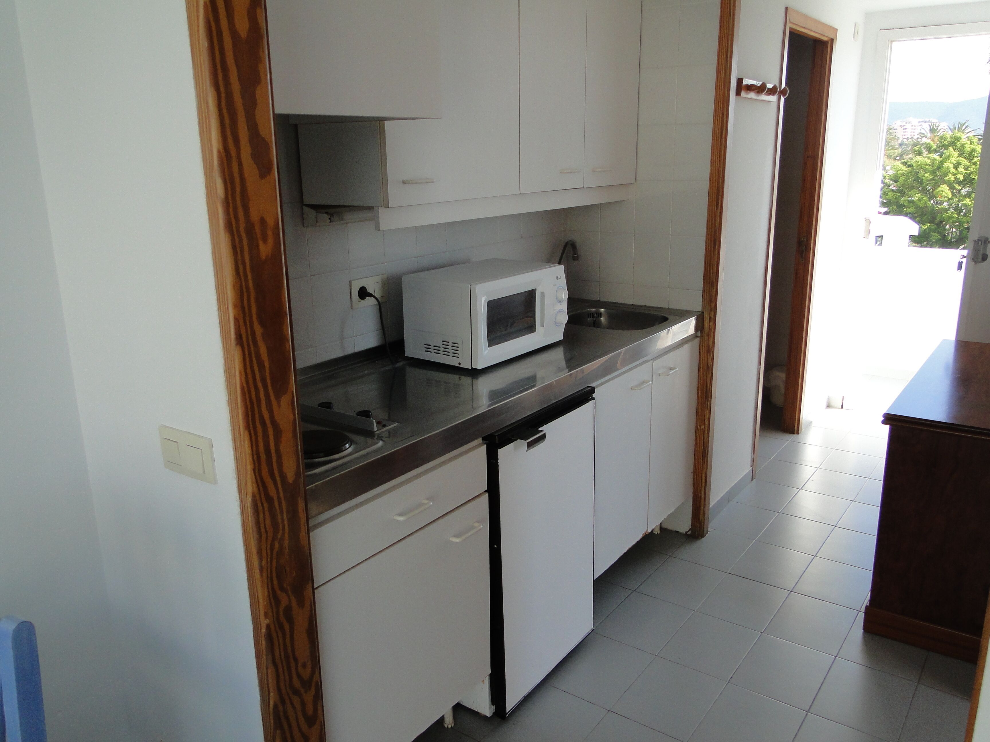 A kitchen with white cabinets, a microwave, and a stainless steel sink.
