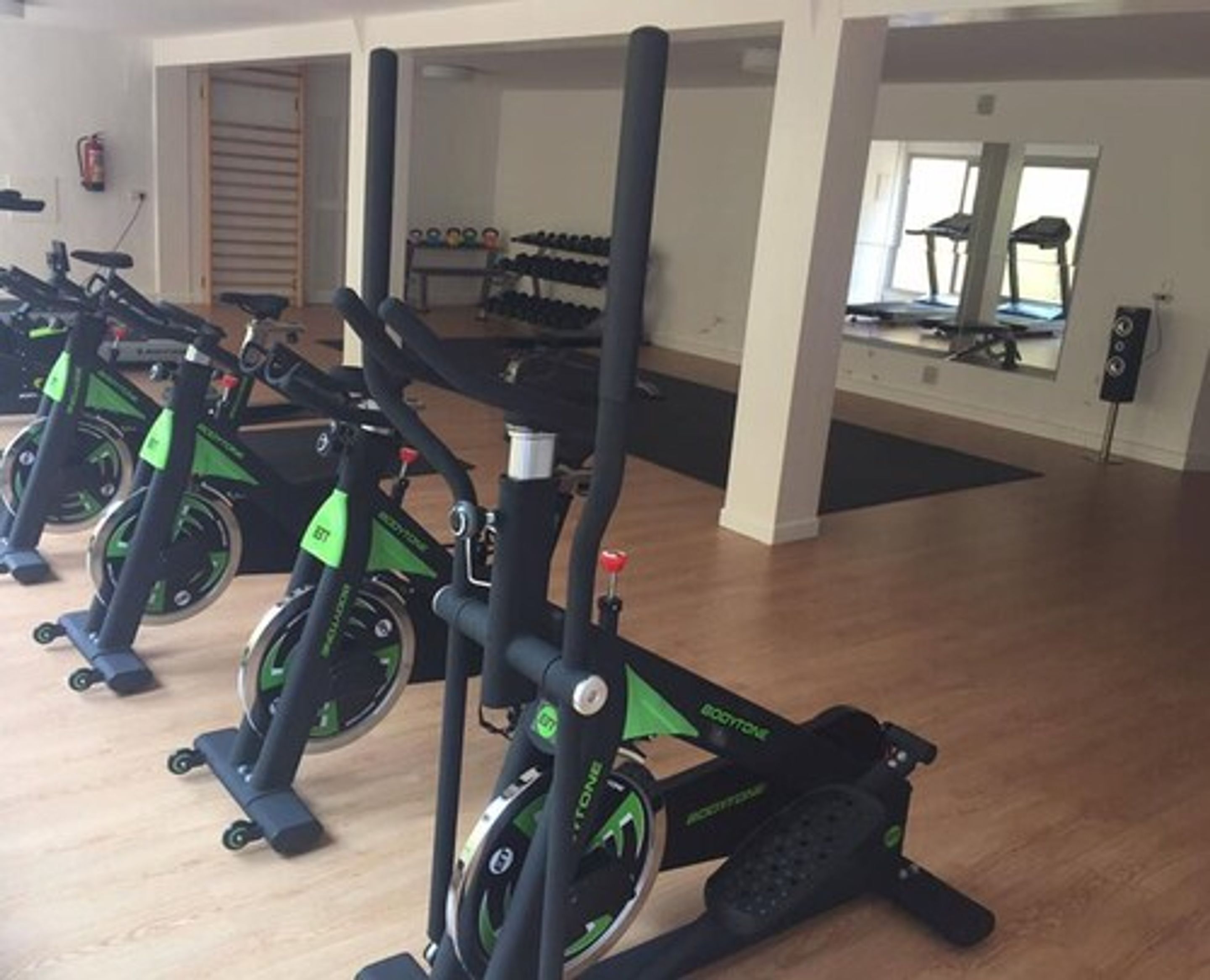 A gym with stationary bikes, a fire extinguisher, and a mirror reflecting the room.
