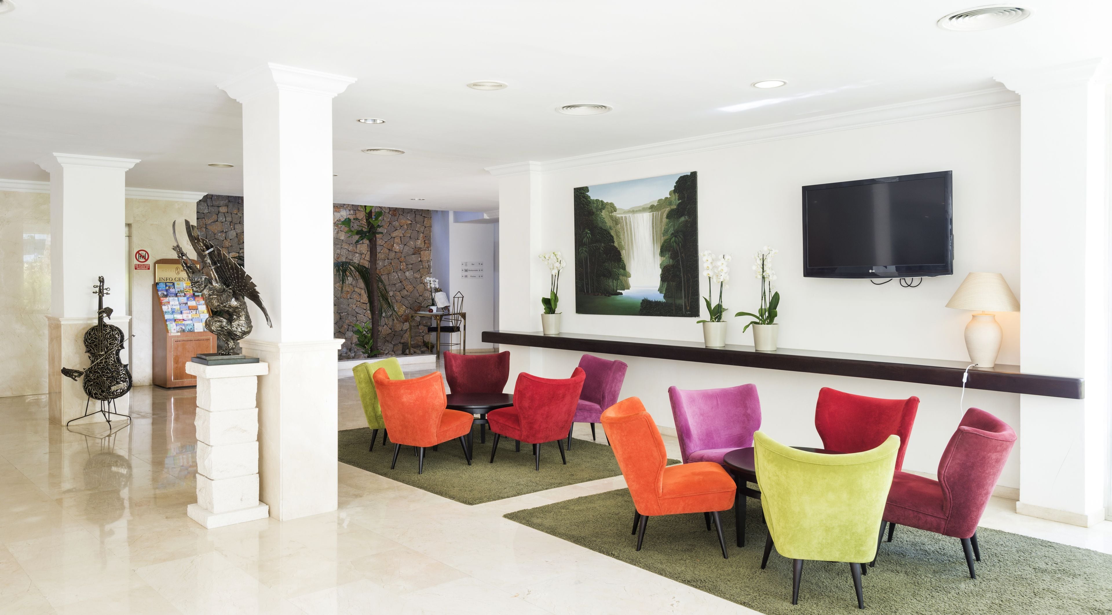 A lobby with a reception desk, colorful chairs, a TV, and a stone wall.
