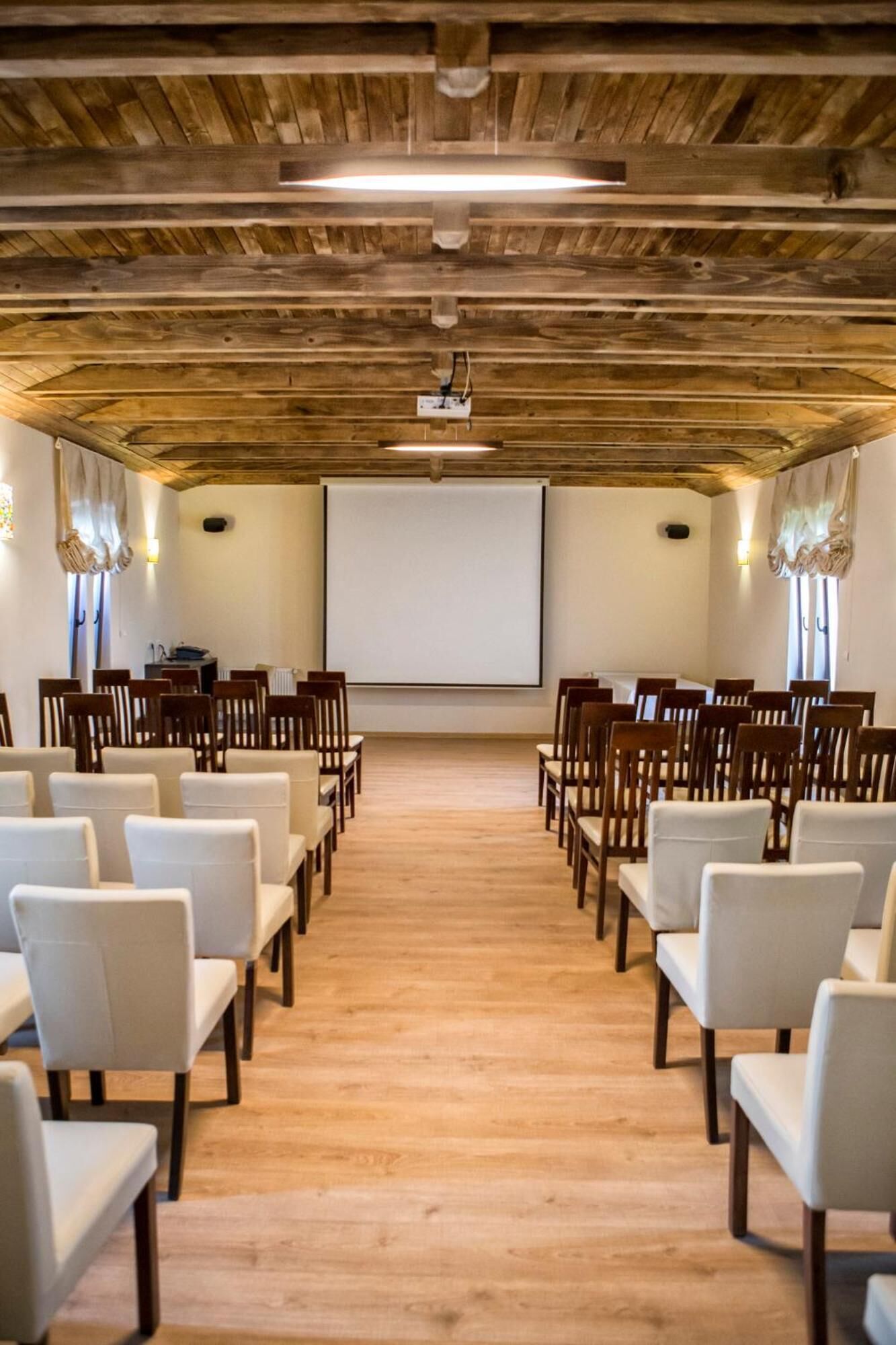 A conference room with wooden ceiling beams, white chairs, and a projector screen.