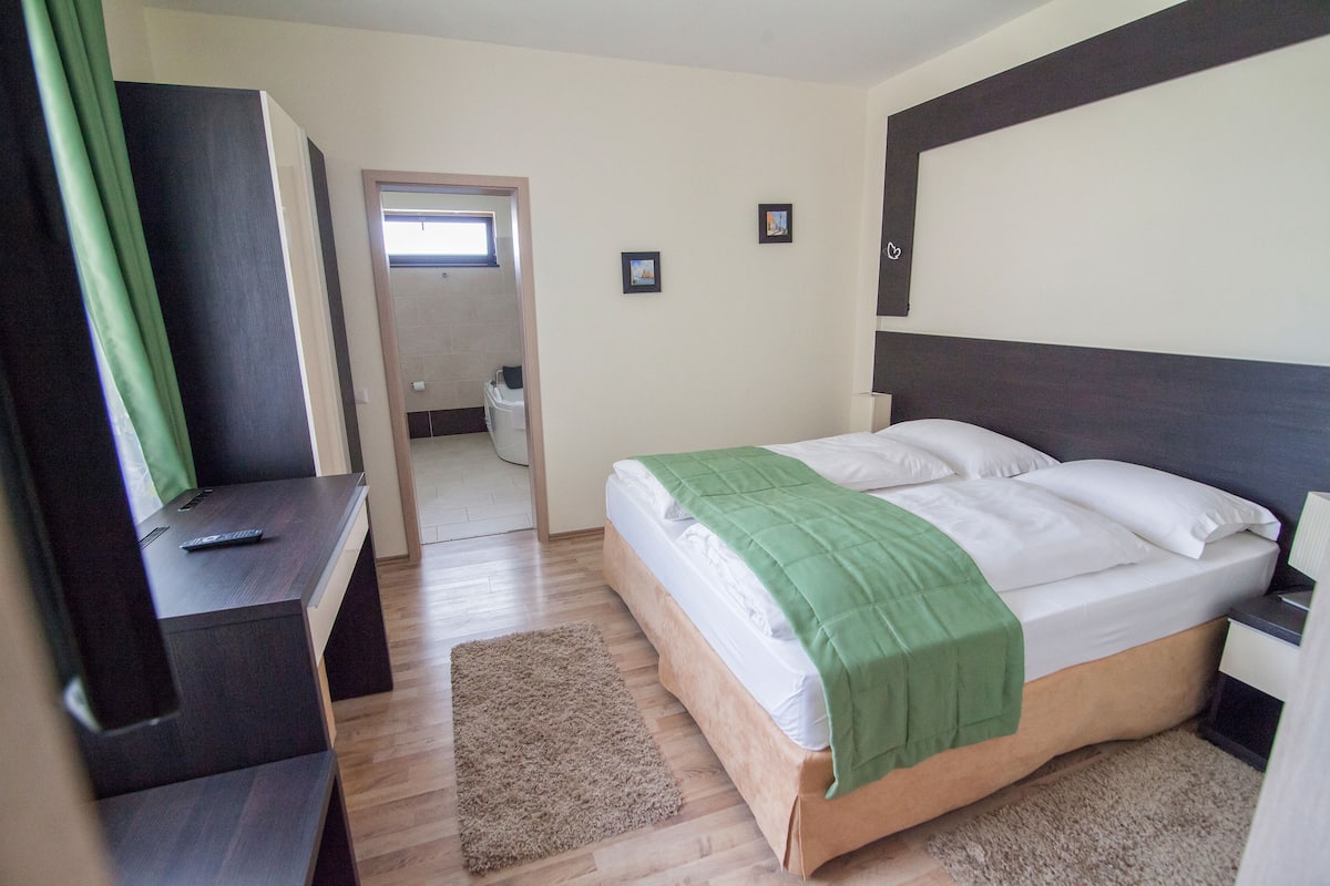 A bedroom with a bed, a desk, and a chair. There is a door leading to a bathroom.